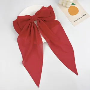 Detailed close-up of a large red chiffon bow hair clip with elegant long streamers.