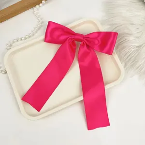 Detailed view of a hot pink satin bow hair clip with long streamers on a white tray