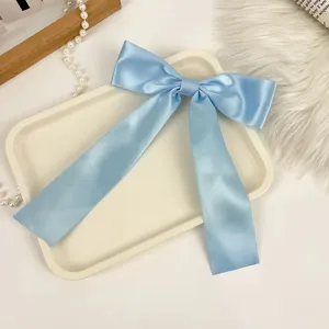Detailed close-up of a light blue satin bow hair clip with elegant long ribbons on a tray