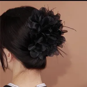 Detailopname van een luxe zwarte stoffen bloemen haarklem met veren op een model