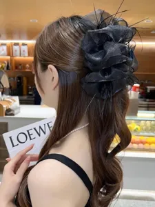 Detailed macro view showing the texture of a black mesh bubble hair clip with feathers