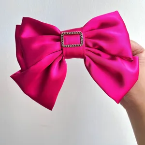 Close-up of a vibrant magenta satin bow hair clip with a gold chain buckle detail.