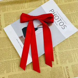 Large red satin ribbon bow hair clip with long tails on vintage background