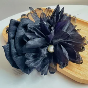 Primo piano di elegante fermaglio a pinza a fiore nero 3D con perla al centro.