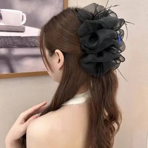 Close-up of large black mesh hair claw clip with feather details on model's hair.