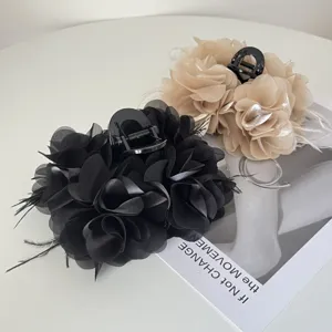 Detail van elegante stoffen bloemenhaarklemmen met verenaccenten in zwart en beige.