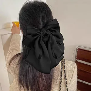 Detail of an oversized black textured chiffon bow hair claw clip styled in a half-updo