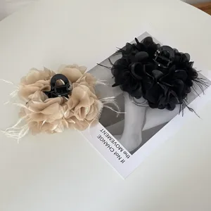 Detail van een elegante stoffen bloem haarklem met veren in zwart en beige.
