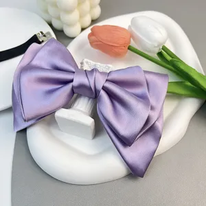 Detailed close-up of a elegant purple satin bow hair clip on a white decorative tray
