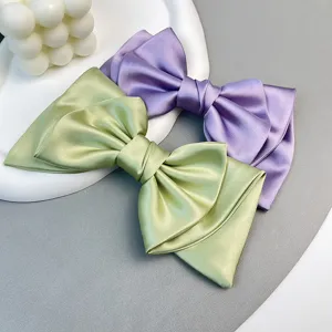 Detail view of elegant satin bow hair clips in luxury green and purple fabric