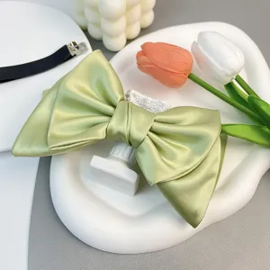 Detail view of a light green satin bow hair clip with a luxurious silky texture and shine.