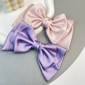 Close-up of two elegant double-layered satin bow hair clips in pink and purple