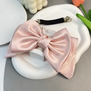 Detailed view of a large pink satin bow hair clip featuring a silver spring fastener clip