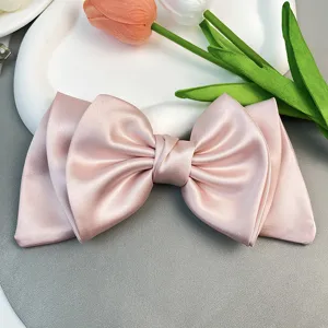 Detailed view of an elegant pink satin bow hair clip styled with tulips on a white tray