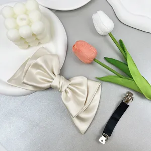 Detail of champagne satin bow hair clip showing front fabric and back alligator clip.