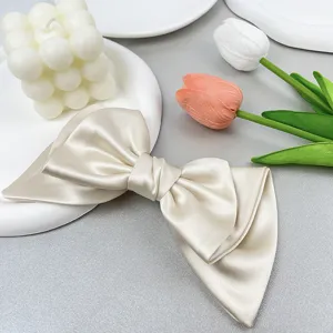 Detailed close-up showing the smooth satin texture of the champagne bow hair clip.