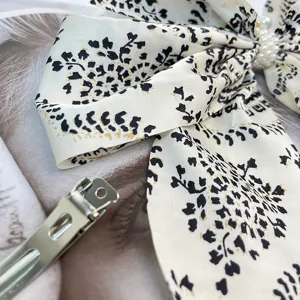Close-up of elegant satin bow hair clip with pearl detail and leopard pattern print