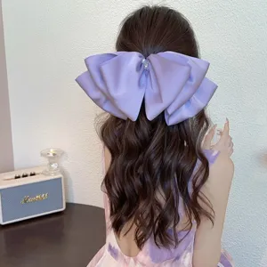 Close-up of oversized purple satin bow hair clip with pearl rhinestone detail