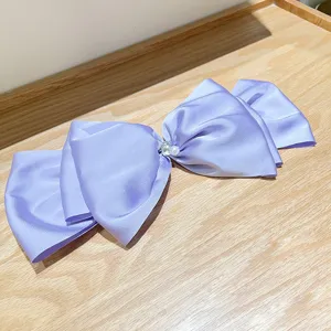 Detailed view of a large lavender satin bow hair clip with pearl and rhinestone accents.