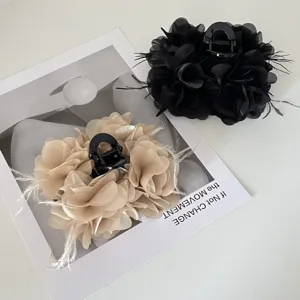 Detailopname van elegante haarklemmen met zwarte en beige stoffen bloemen en veren.