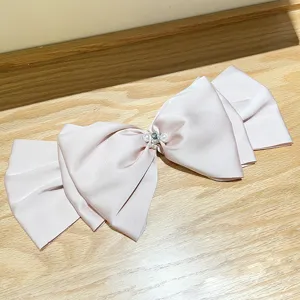 Detail view of large pale pink satin bow hair clip featuring pearls and a sparkling crystal