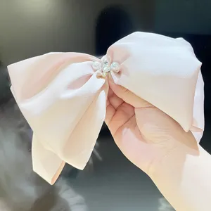 Detailed close-up of a large pale pink satin bow hair clip with pearls and crystals