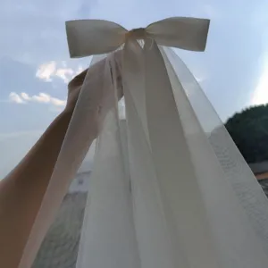 Close-up of ethereal white tulle bow hair veil held against a clear sky background