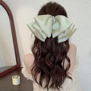 Close-up view of an oversized sage green pearl satin bow hair clip on wavy hair