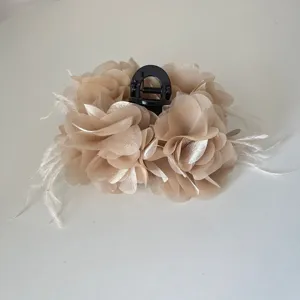 Detailopname van een elegante haarklem met beige stoffen bloemen en witte veren versiering