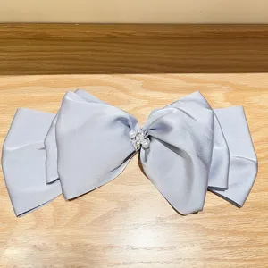 Close-up of a large blue satin bow hair clip with pearl and rhinestone center detail