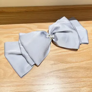 Close-up of an oversized light blue satin bow hair clip with pearls and rhinestones.