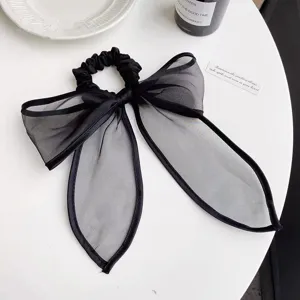 Detailopname van een elegante zwarte scrunchie met strik van fijne organza-textuur.