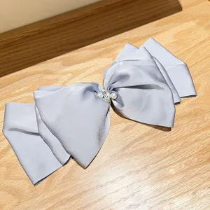 Detailed view of large silver satin bow hair clip with pearl and rhinestone center