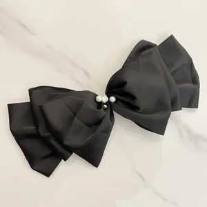 Detail of a large black satin bow hair clip with elegant pearl and crystal embellishment.