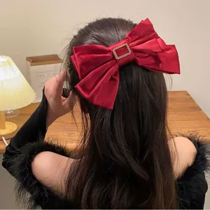 Close-up of a large red satin bow hair clip with a gold buckle worn by a model