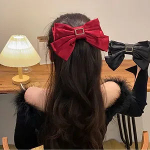 Burgundy and black large satin bow hair clips with gold buckle shown on long wavy hair.