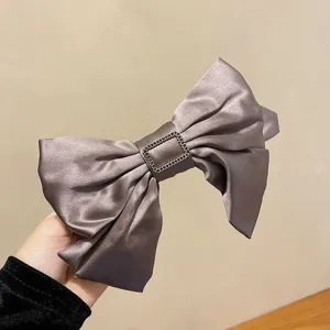 Close-up view of an elegant taupe satin bow hair clip with a rectangular metal buckle