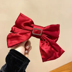 Close-up of red three-layer satin bow hair clip showing metallic buckle texture