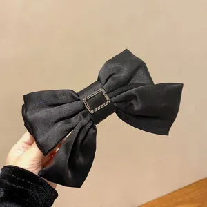 Close-up detail of elegant black satin bow hair clip featuring a gold metal buckle decoration