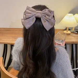 Back view of a large taupe satin bow hair clip with gold buckle on long wavy brown hair