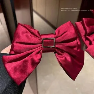 Close-up of elegant red satin three-layer bow hair clip with decorative gold buckle detail