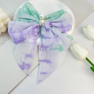 Gros plan sur une pince à cheveux nœud en mousseline plissée avec perle et motif tie-dye