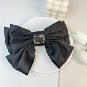 Close-up detail of large black satin triple-layered bow hair clip with a gold buckle