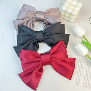 Detail of three large satin triple-layered bow hair clips in purple, black, and red colors.