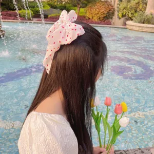Fille portant une pince à cheveux en mousseline plissée rose avec perles près d'une fontaine.