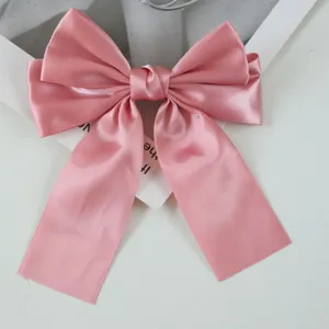 Close-up detail of a sweet pink satin ribbon bow hair clip with glossy texture.