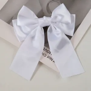Close-up detail of a white satin ribbon bow hair clip on a minimalist background.