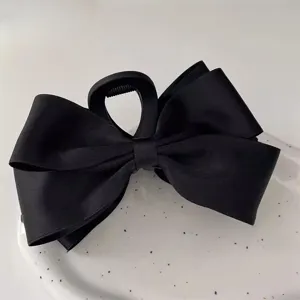Detailed view of an elegant black satin ribbon bow hair claw clip displayed on a white plate.