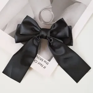 Close-up detail of a minimalist black satin ribbon bow hair clip on a white background