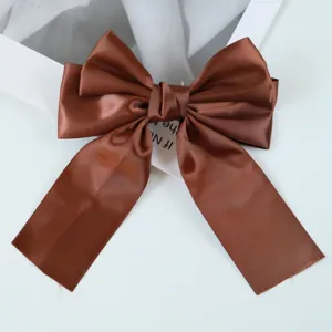 Macro shot of a shimmering brown satin ribbon bow hair clip on a minimal white background